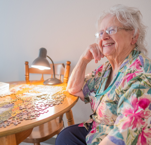 elderly woman sitting at a table putting a puzzle together while looking and smiling at someone next to her off camera at parsons house omaha