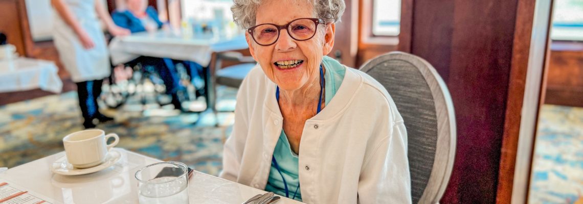 a senior living resident with gray hair, glasses, and a white sweater sitting at a table.